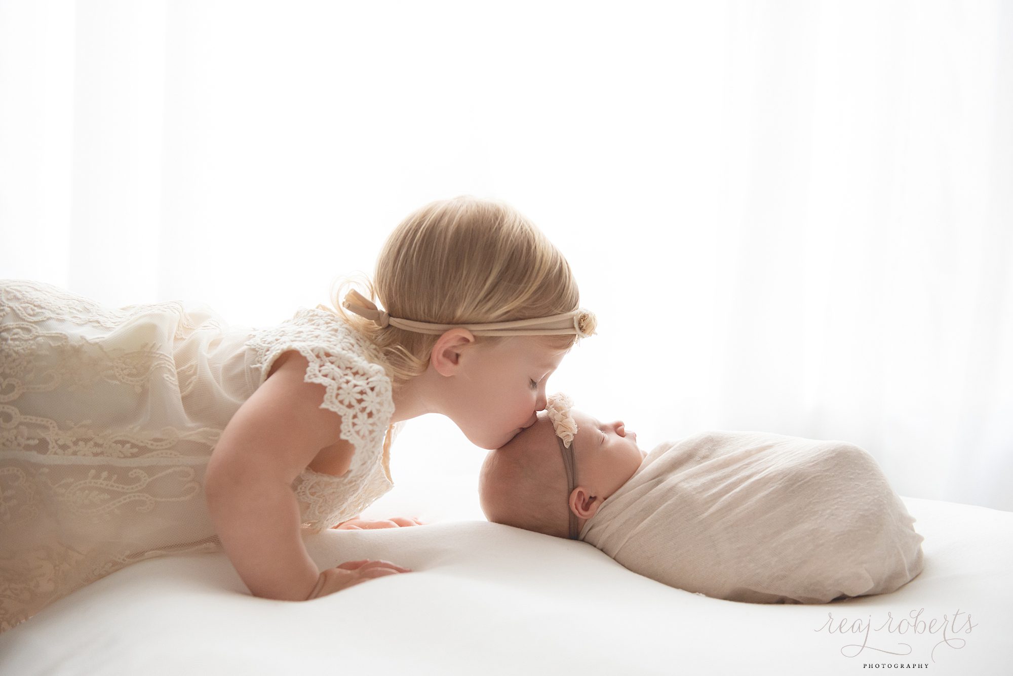 newborn baby girl being kissed by big sister | Reaj Roberts Photography