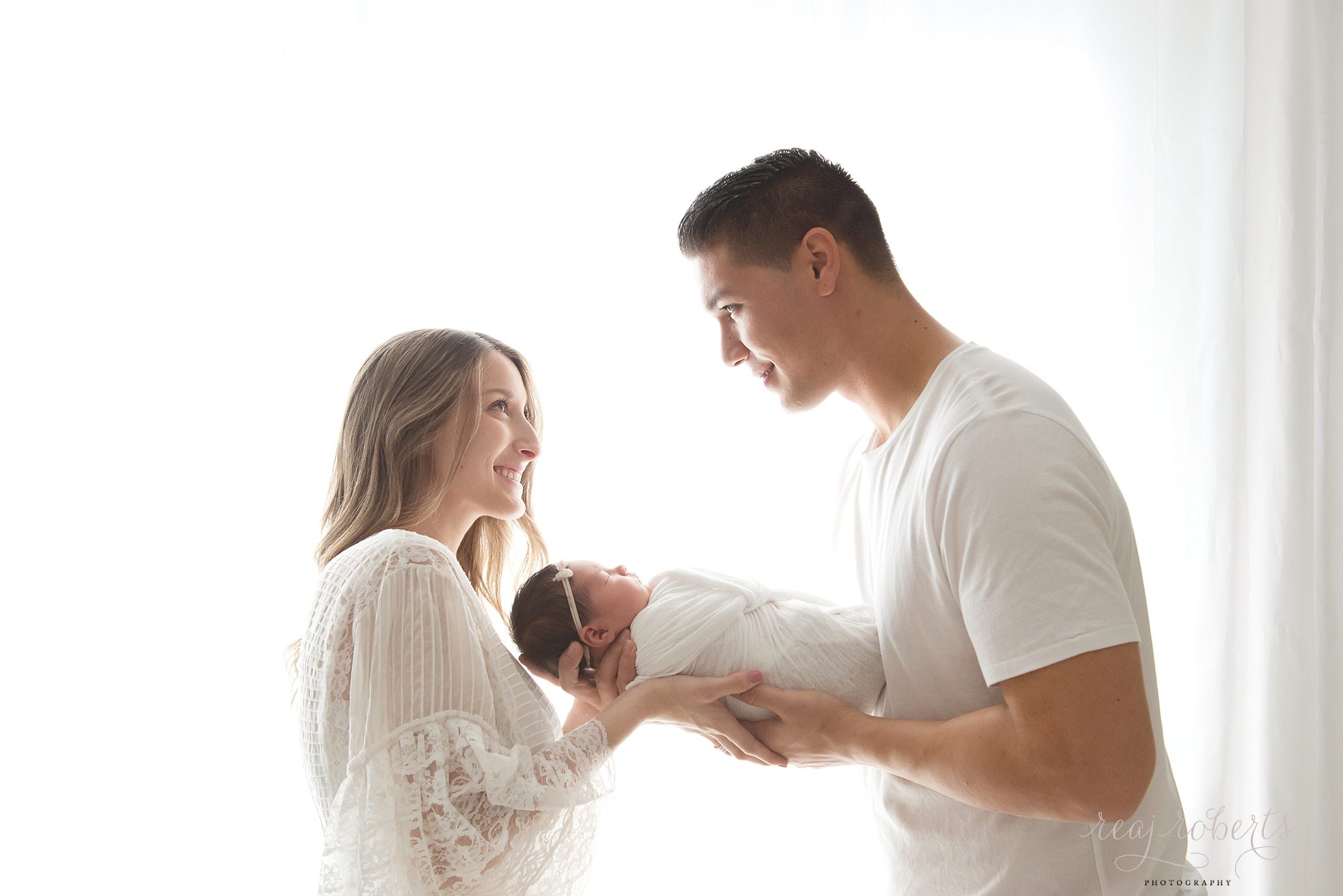 Chandler Baby Photographer | Reaj Roberts Photography | happy parents holding newborn in front of window