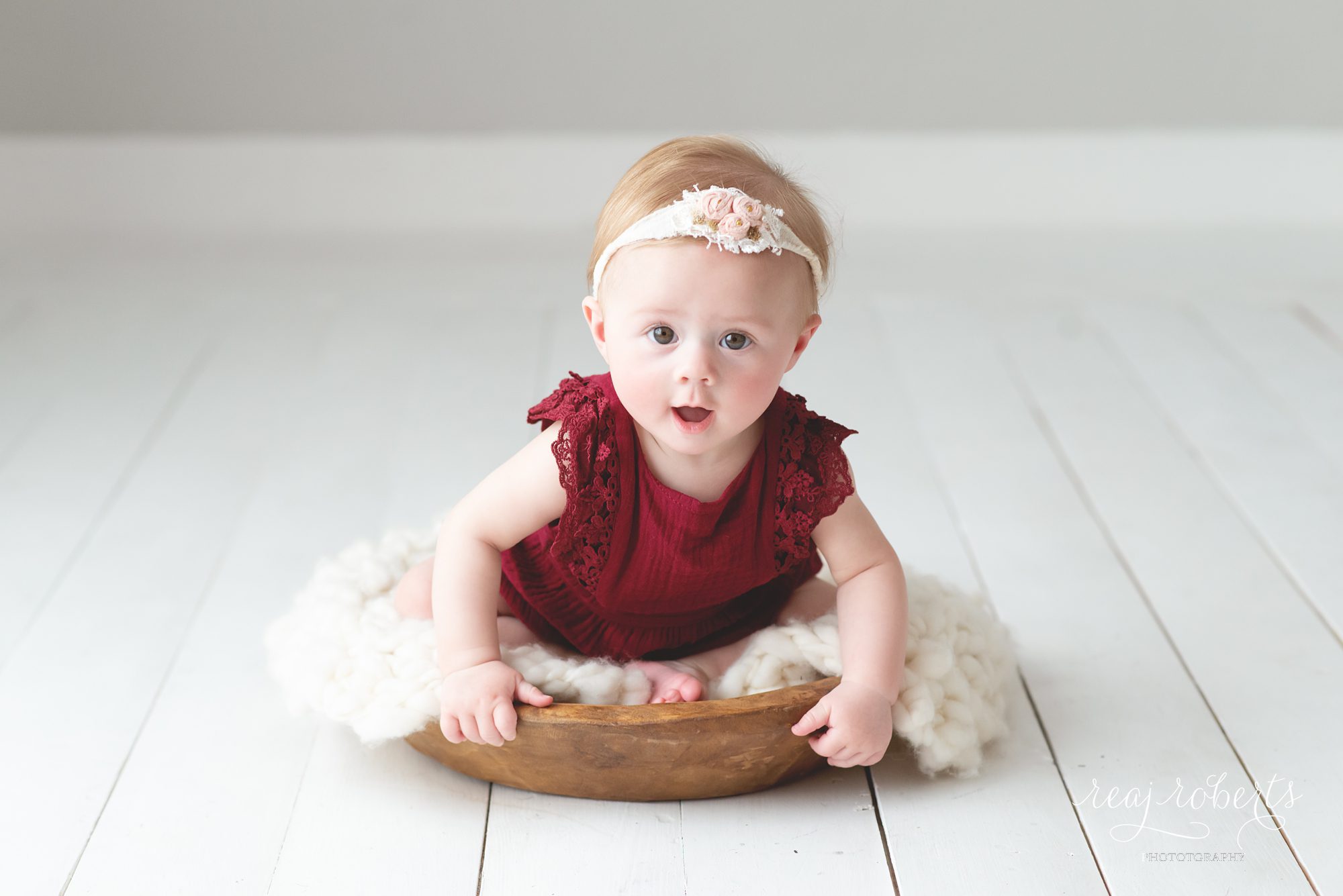6 month baby girl in cranberry red romper in bowl, baby Christmas photo ideas | Reaj Roberts Photography