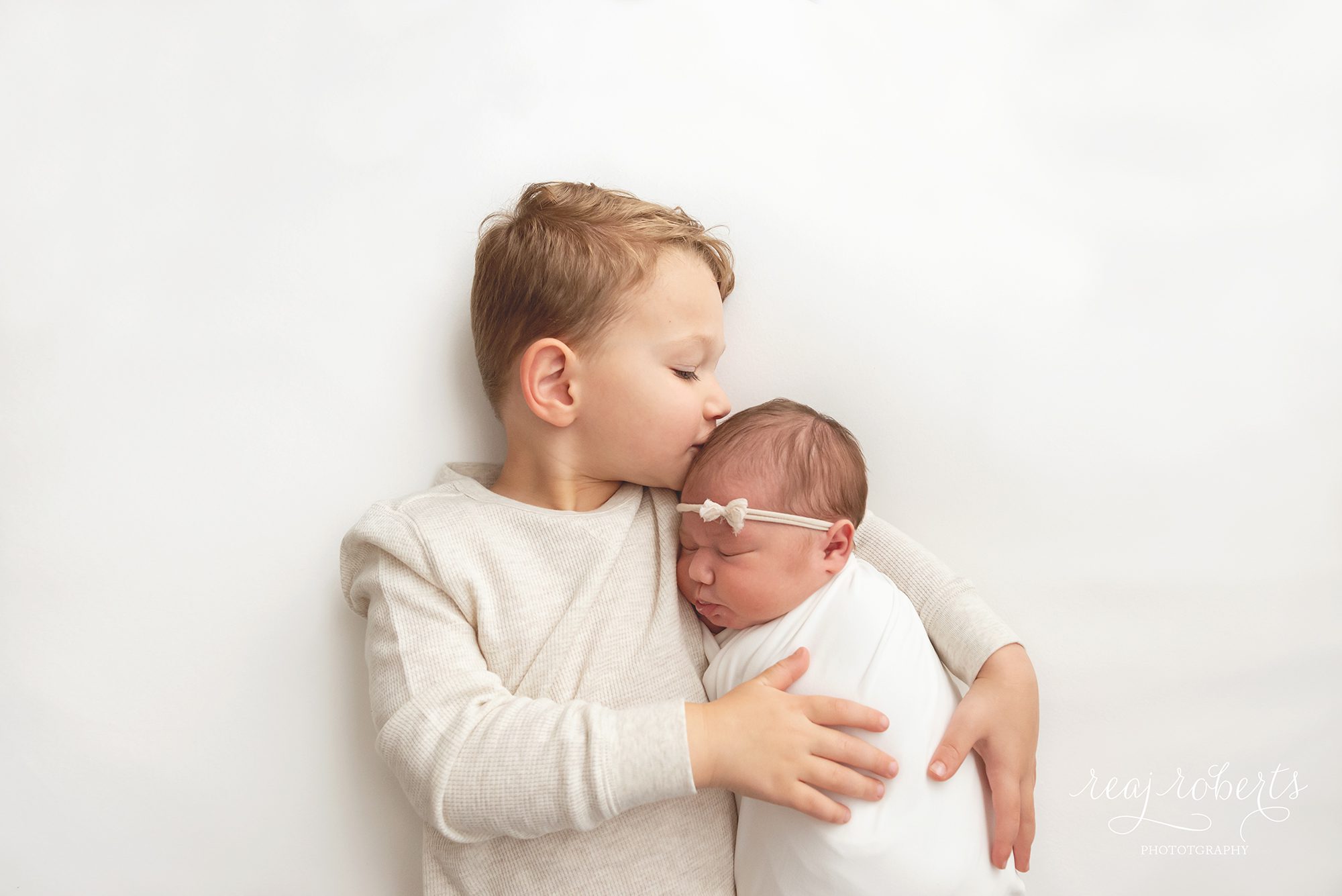 newborn baby poses with older siblings, brother kissing baby sister on head | Reaj Roberts Photography
