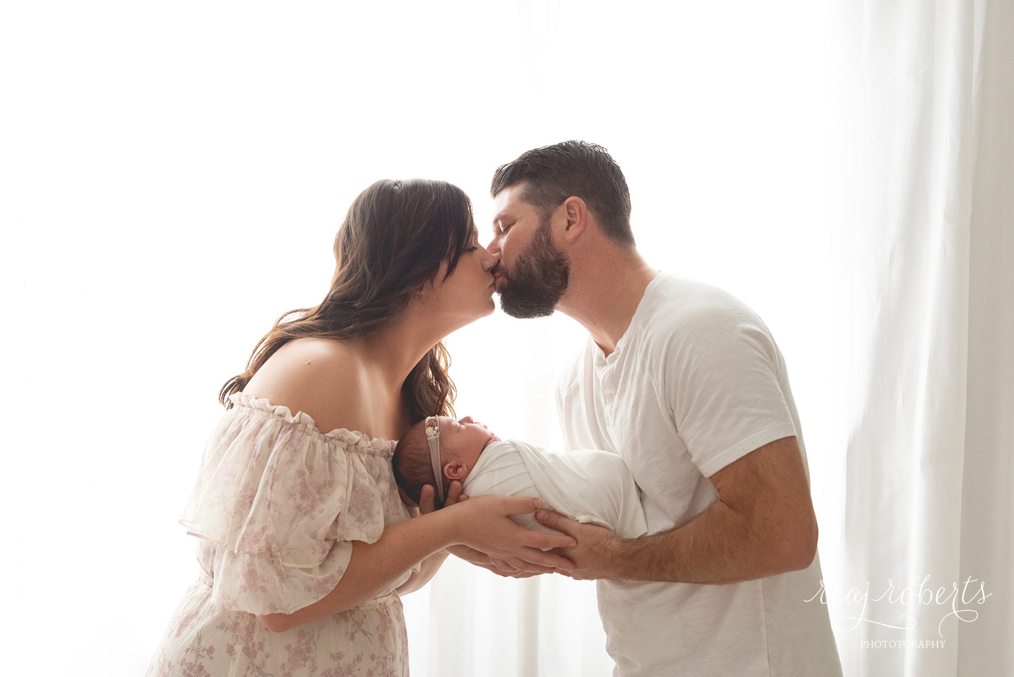 newborn photography parents holding baby in front of white window | Reaj Roberts Photography