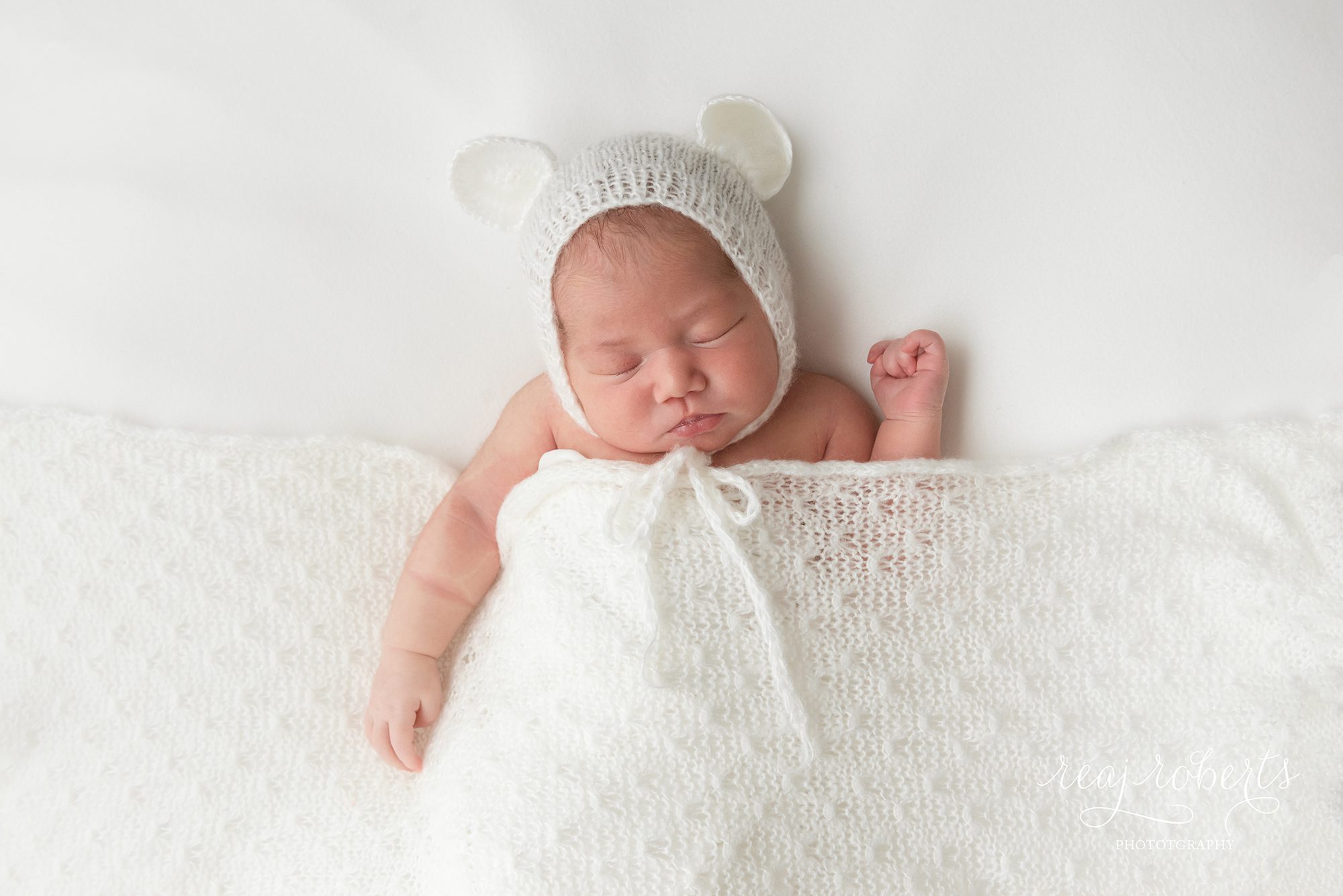newborn baby tucked in white knit blanket with knit teddy bear hat | Reaj Roberts Photography