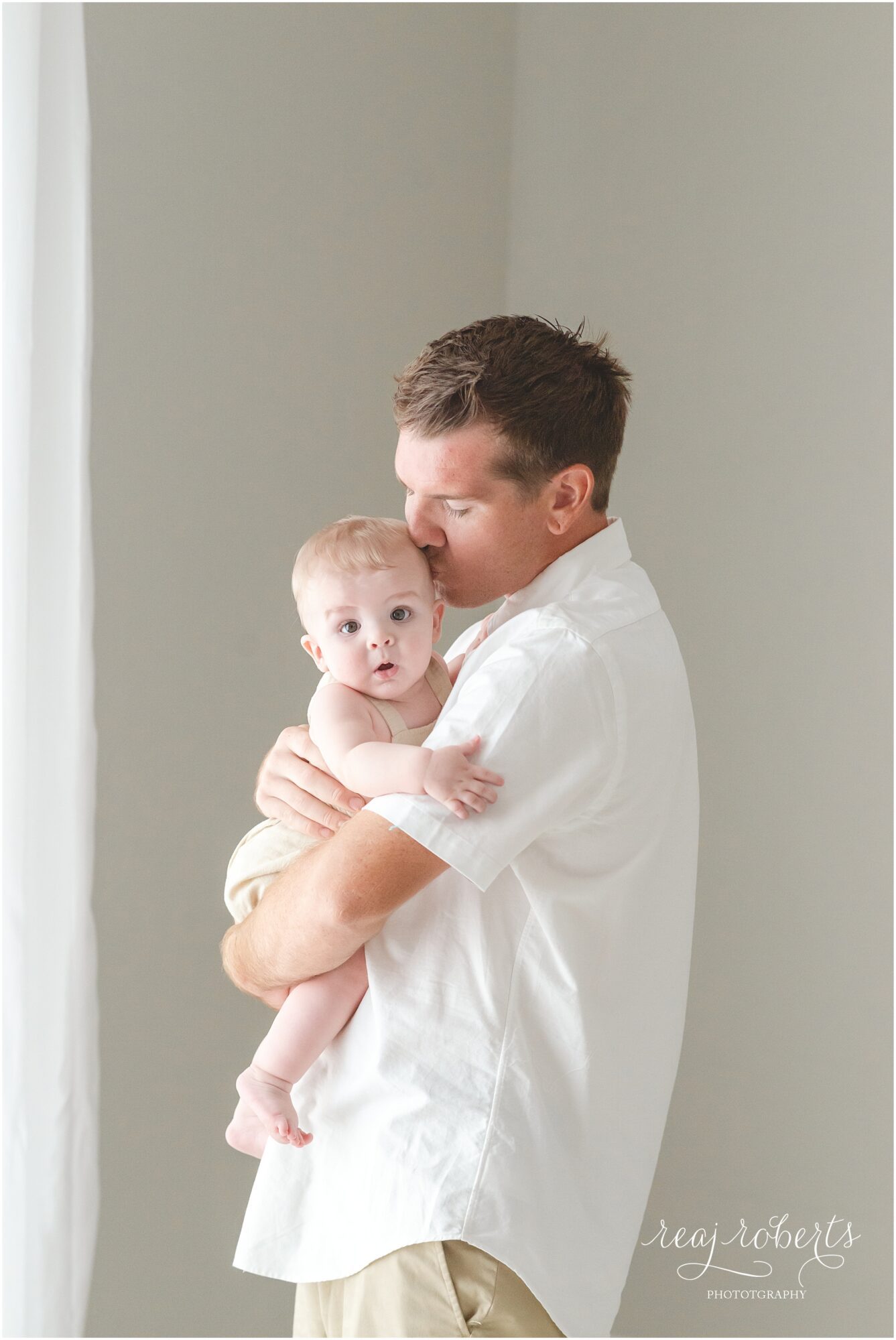 Father wearing white shirt kissing 6 month old son wearing tan romper | Reaj Roberts Photography