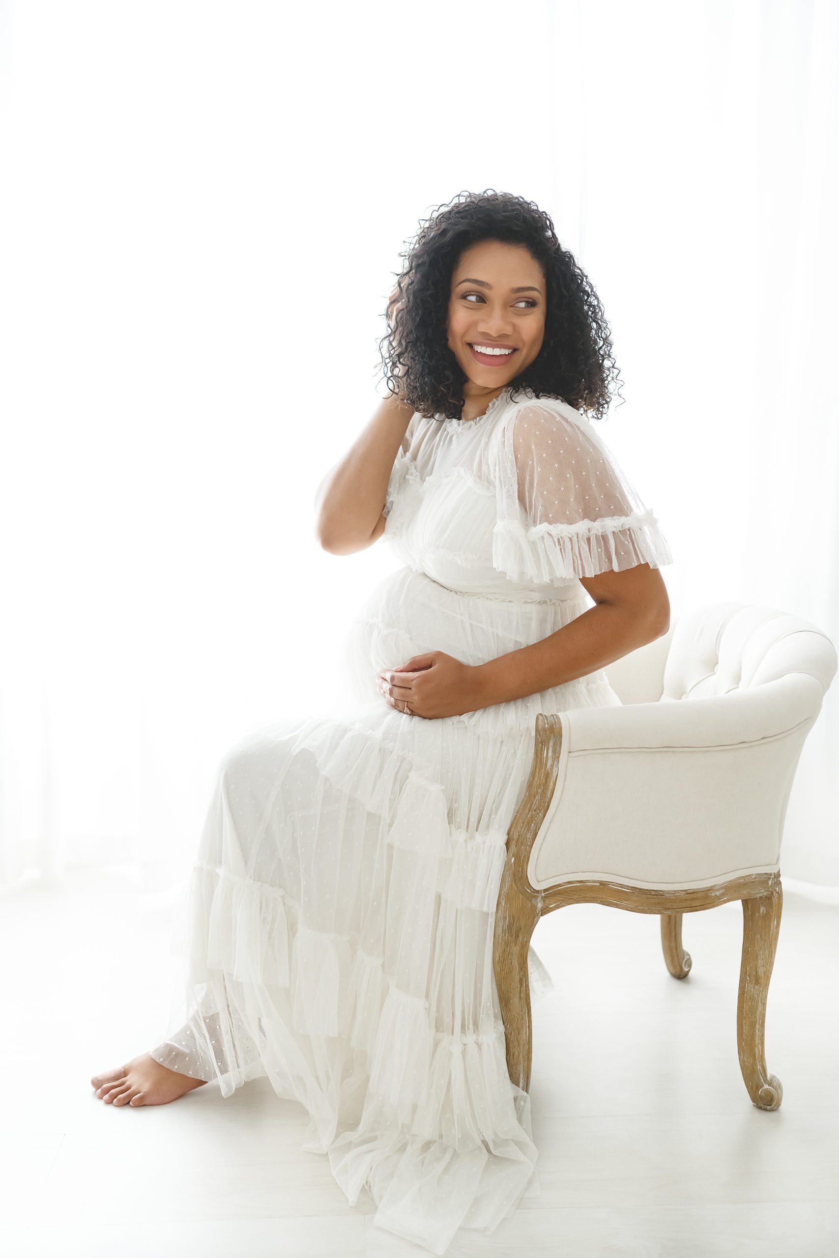 pregnant woman wearing white lace dress sitting in chair ©Reaj Roberts Photography