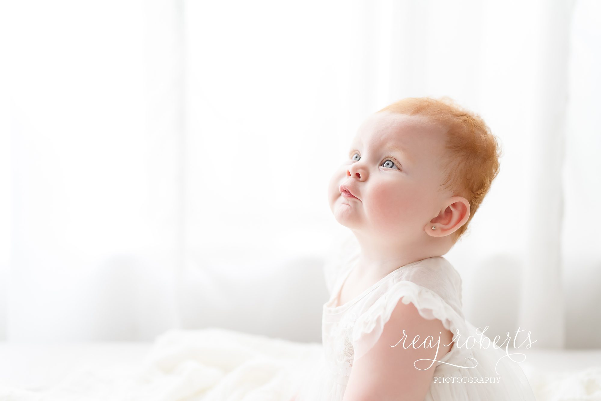 baby with blue eyes red hair in white dress © Reaj Roberts Photography
