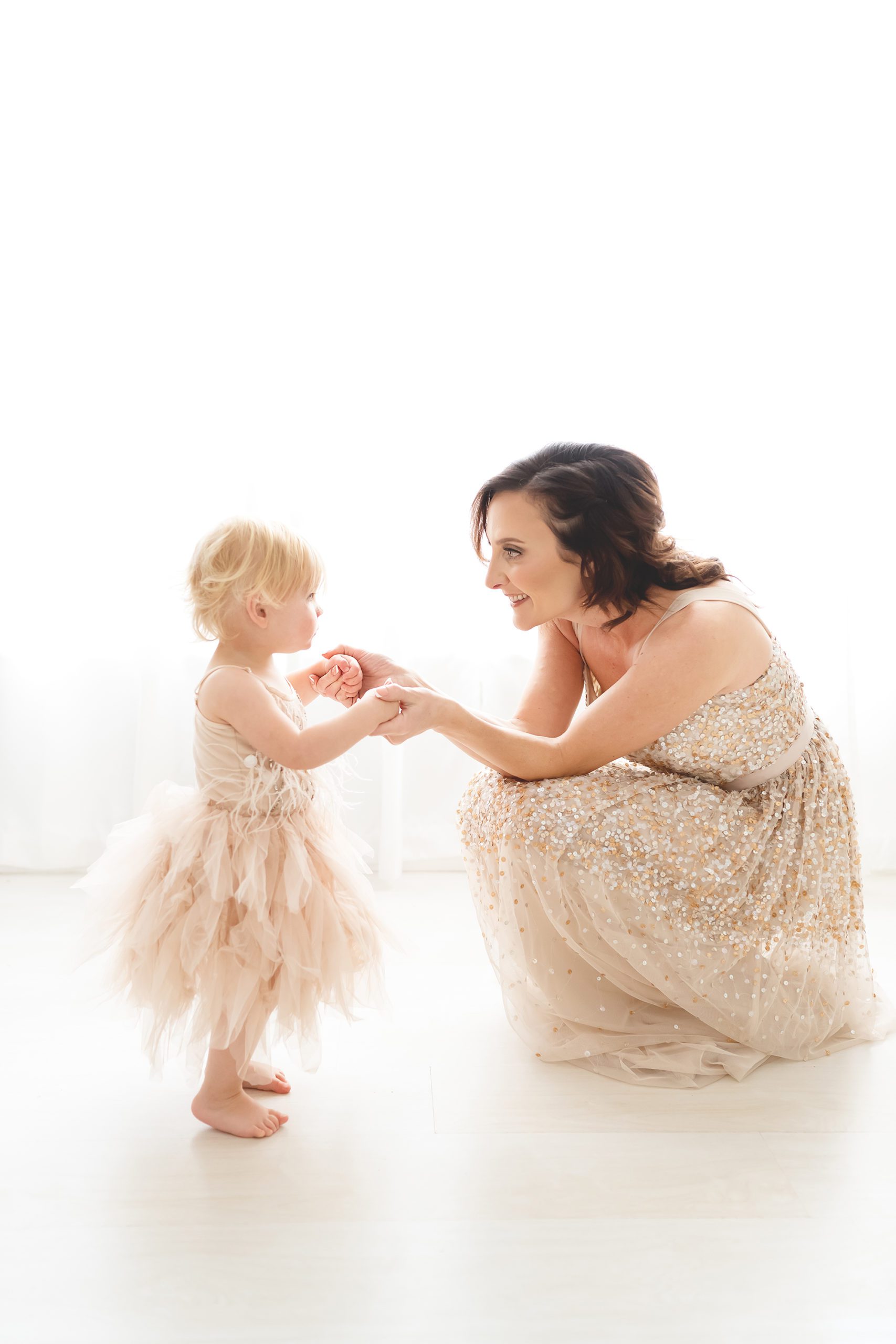 Mom and baby girl standing up in gold sparkly dresses